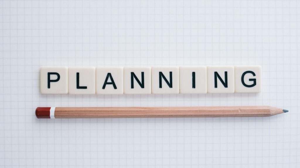 Overhead shot of letter tiles spelling 'planning' with a pencil on graph paper.